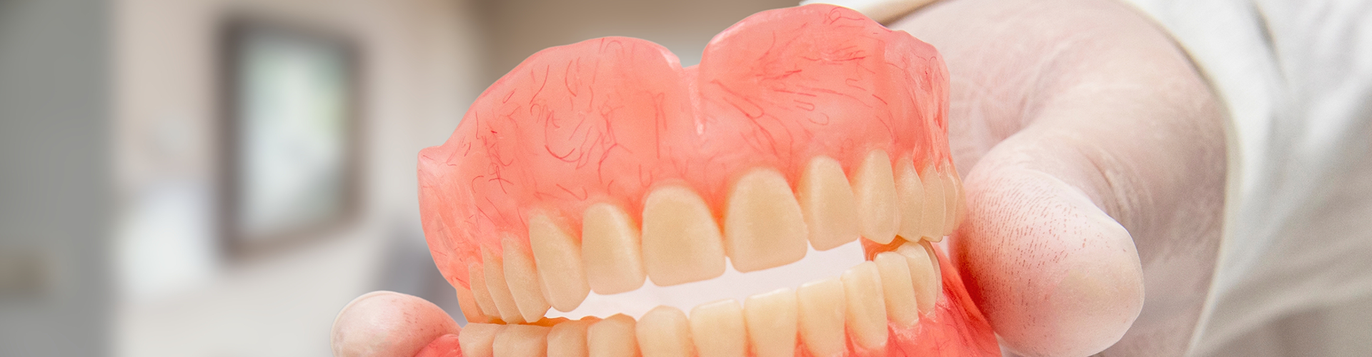gloved hand holding upper and lower dentures